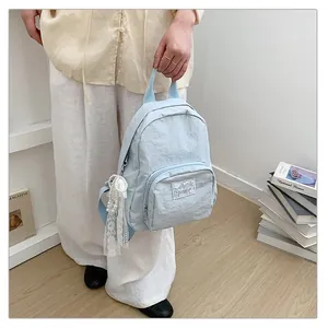 Close-up of a light blue minimalist backpack with lace pearl keychain detail