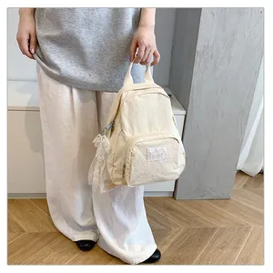 Model holding a minimalist cream-colored mini backpack in a clean lifestyle setting