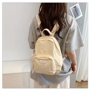 Back view of a minimalist beige student backpack on a model in a casual indoor setting
