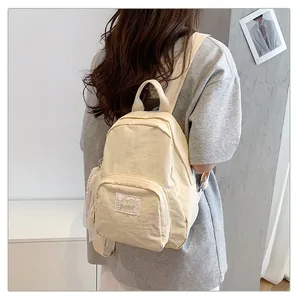 Close-up detail of a minimalist cream-colored backpack worn by a female model in a casual setting