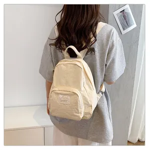 Back view of a minimalist cream-colored canvas backpack worn by a female model
