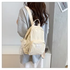 Girl wearing a cream-colored minimalist nylon backpack with a decorative lace charm.