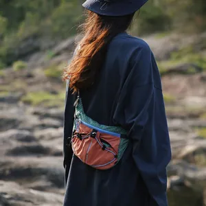 Zweifarbige Outdoor-Umhängetasche für Reisen, getragen von einem Model in felsiger Natur.