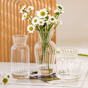 Detailansicht von drei klaren gerippten Glasvasen mit Gänseblümchen für elegante Deko.