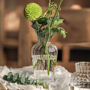 Detailansicht einer Vintage-Glasvase mit Rillen und frischen grünen Blumen auf Gaze.