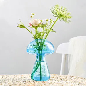 Vue détaillée d'un vase champignon en verre bleu avec composition florale sur natte.