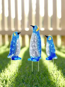 Detailansicht von drei verschieden großen Pinguin-Gartensteckern auf einem sonnigen Rasen.