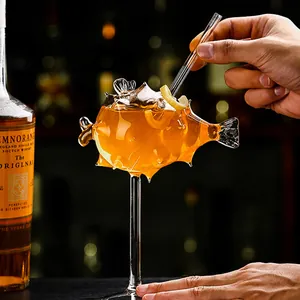 Copa de cóctel única con forma de pez globo con bebida naranja y una pajita de cristal transparente