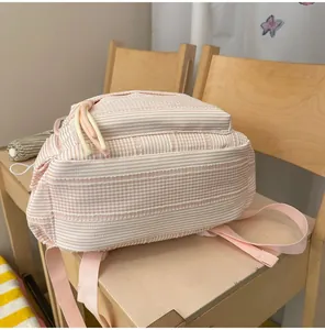 Close-up side view of a pink and white striped school backpack for students on a wooden chair