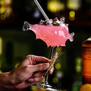 Copa de cóctel rosa única con forma de pez globo sostenida a mano en un bar chic