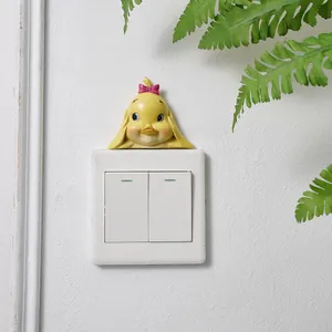 Cute handmade resin yellow duck figurine decoration placed above a white wall switch