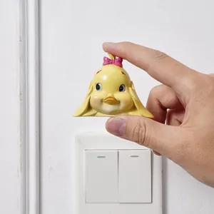 Close-up of a hand holding a cute yellow duck resin sticker above a white light switch