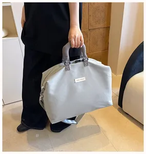 Persona che tiene una grande borsa da viaggio fitness grigio chiaro con manici e tracolla.