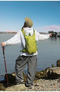 Donna con zaino da trekking ultraleggero verde lime vicino all'acqua con bastoncini.