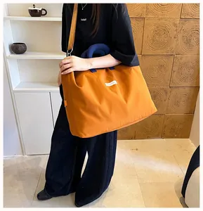 Modella che indossa una grande borsa da viaggio arancione con manici blu in un interno.