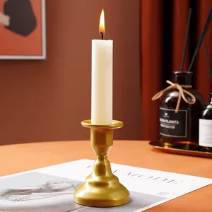 Elegant gold metal candlestick holder with a lit white candle in a warm lifestyle setting