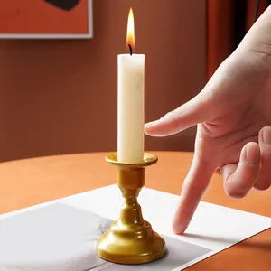 Golden iron candlestick holder with lit white candle, detail view with hand for scale