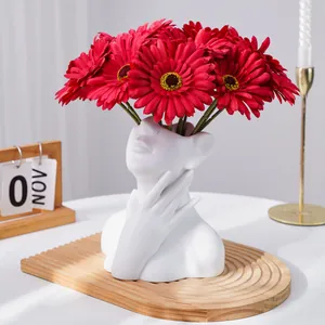 Detalle de moderno jarrón busto de cerámica blanca con gerberas artificiales rojas