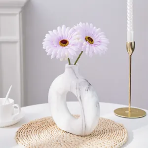 Jarrón moderno de mármol blanco con margaritas lavanda sobre un mantel individual