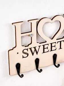 Nahaufnahme des hölzernen HOME SWEET Schlüsselbretts mit geschnitzten Buchstaben und Haken