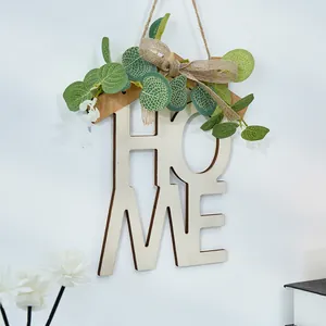 Letrero de madera HOME decorativo con hojas de eucalipto en una pared blanca