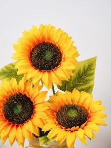 Nahaufnahme eines künstlichen Sonnenblumenstraußes mit drei Köpfen und grünen Blättern