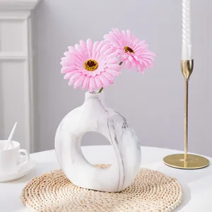 Detalle de margaritas gerberas artificiales rosas en jarrón circular de mármol cerámico