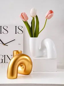 Vases modernes en résine courbée blanc et or avec tulipes roses sur un bureau minimaliste.