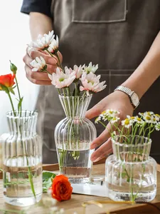 Nahaufnahme einer Person, die Blumen in eine gerippte Glasvase aus Klarglas stellt