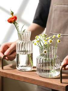 Detail von geriffelten Klarglasvasen mit frischen Gänseblümchen und einer Rose auf Holztablett