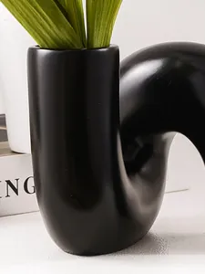 Détail rapproché d'un vase en résine noir minimaliste au design artistique de tuyau incurvé