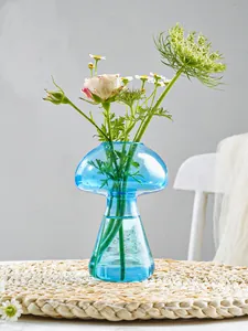 Vue rapprochée détaillée du vase champignon en verre bleu avec des fleurs sur une natte.