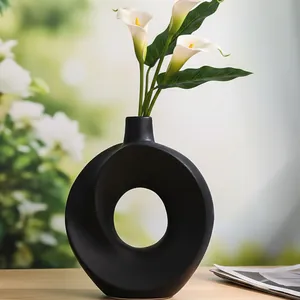 Minimalistische schwarze Keramikvase mit weißen Calla-Lilien auf einem Holztisch