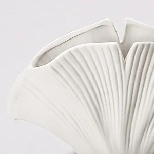 Detailopname van de geribbelde textuur en schelpvormige rand van de witte vaas.