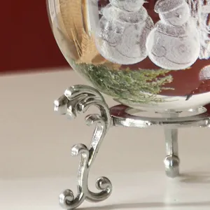 Detalle del soporte plateado y muñecos de nieve en una bola de cristal transparente.