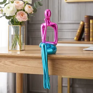 Moderne Harzfigur mit Farbverlauf zeigt eine sitzende Figur mit langen Beinen am Tisch.