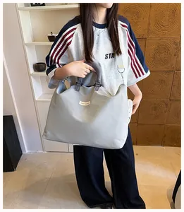 Grande borsa sportiva grigia per viaggi e fitness, indossata da una modella asiatica.
