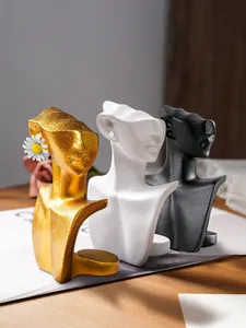 Primo piano di tre sculture a busto astratte in resina nei colori oro, bianco e nero.