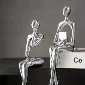 Vista detallada de dos esculturas abstractas plateadas en posición sentada sobre un estante