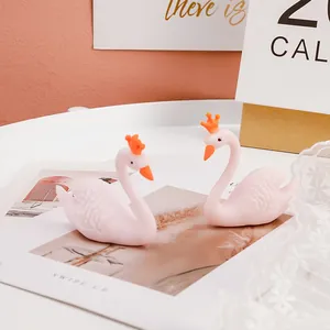 Gros plan de deux figurines de cygnes roses en caoutchouc souple avec couronnes oranges