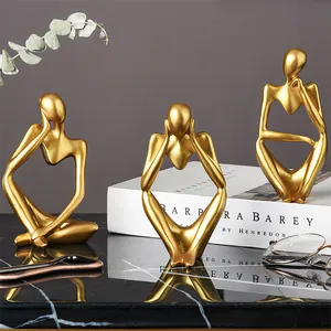 Juego de tres figuras doradas de pensadores abstractos nórdicos en un escritorio.