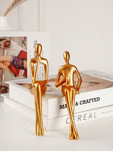 Vue détaillée de deux statues minimalistes en or de personnages abstraits assis sur des livres