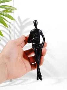 Gros plan d'une figurine humaine abstraite noire tenue à la hand montrant l'échelle