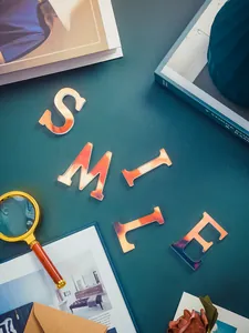 Vue détaillée des lettres en acrylique irisé formant SMILE sur un bureau bleu sarcelle