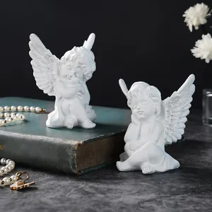 Close-up of two white resin cherub angel statues resting on a vintage green book.