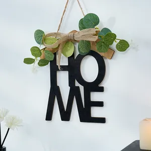 Detalle de adorno de pared HOME de madera con hojas de eucalipto y lazo de arpillera