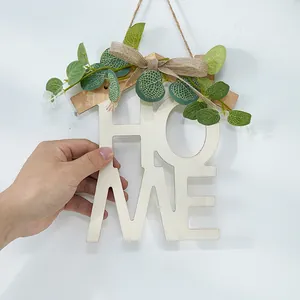 Detalle de un adorno de pared HOME de madera con hojas verdes y un lazo de tela de arpillera.