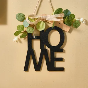 Detalle de decoración de pared HOME en madera rústica con hojas verdes y lazo de yute