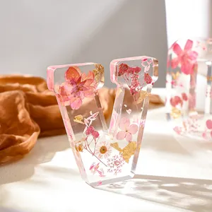 Primo piano di una lettera decorativa V in resina con fiori secchi rosa e scaglie d'oro