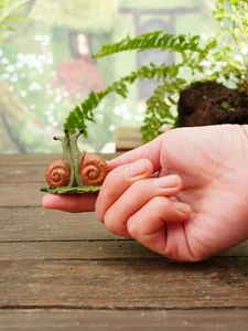 Miniature resin snail figurine held in hand to show small garden decoration scale